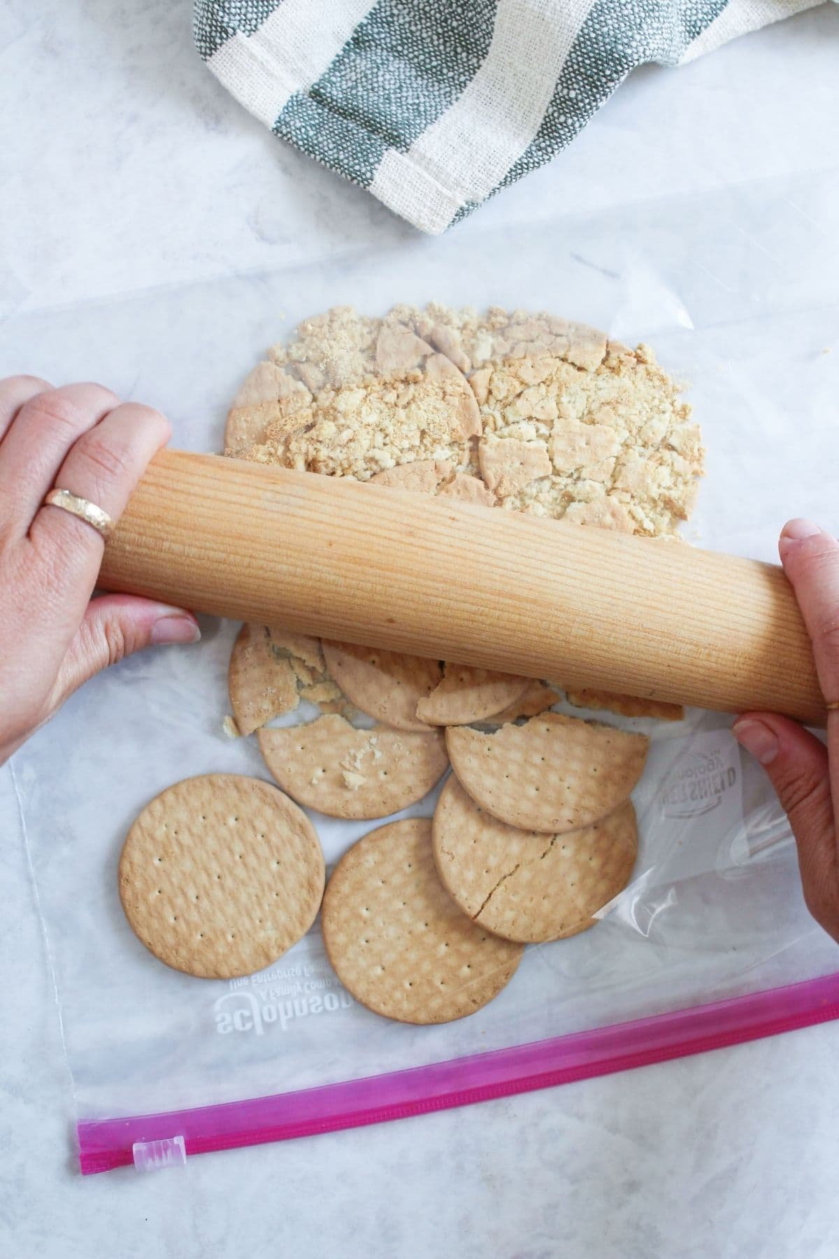 Shortbread cookies being crushed with a rolling pin to create the cobbler topping layer for peach cobbler jam.