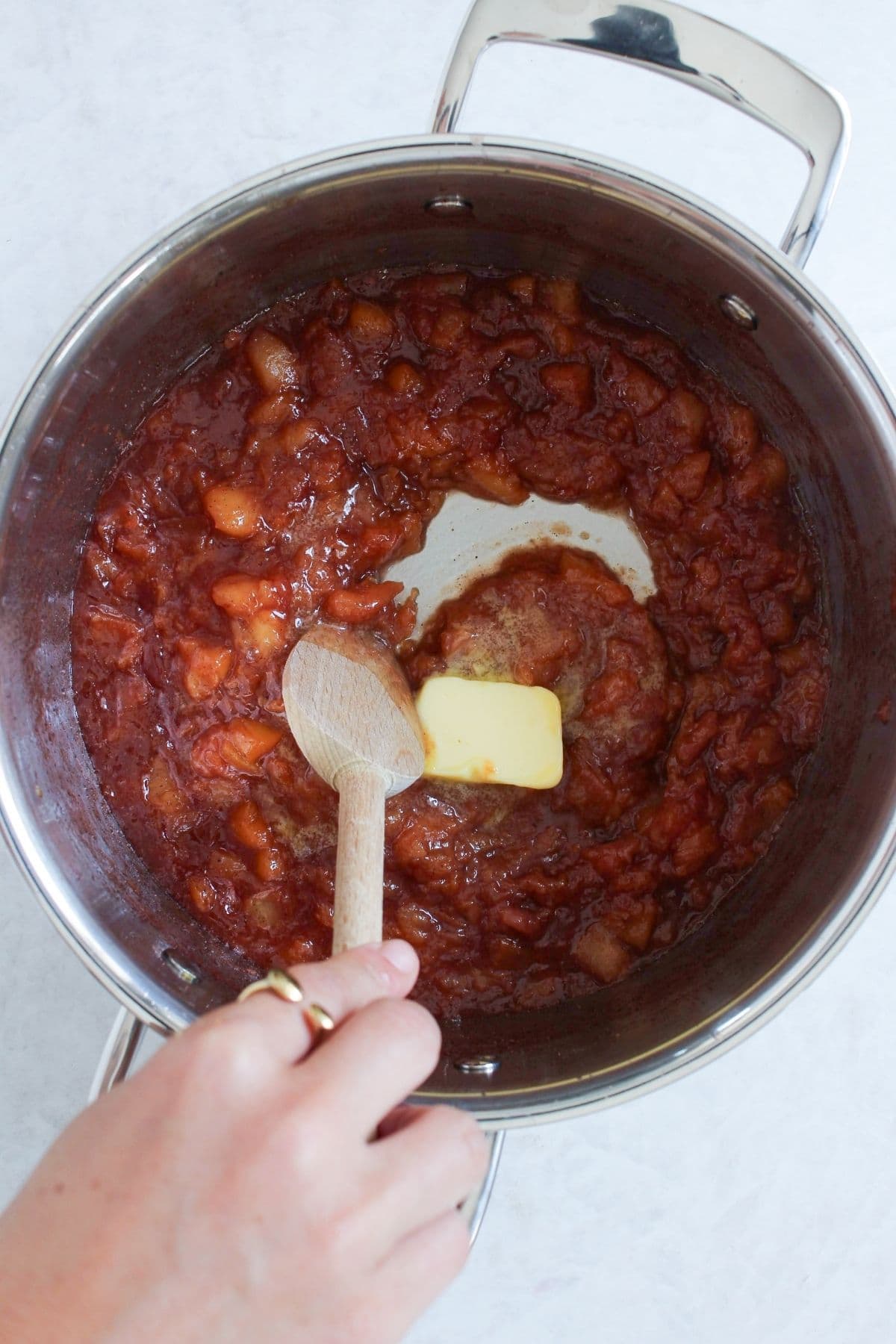 Butter being stirred into a pot of simmered peach cobbler jam to create a rich, glossy finish.