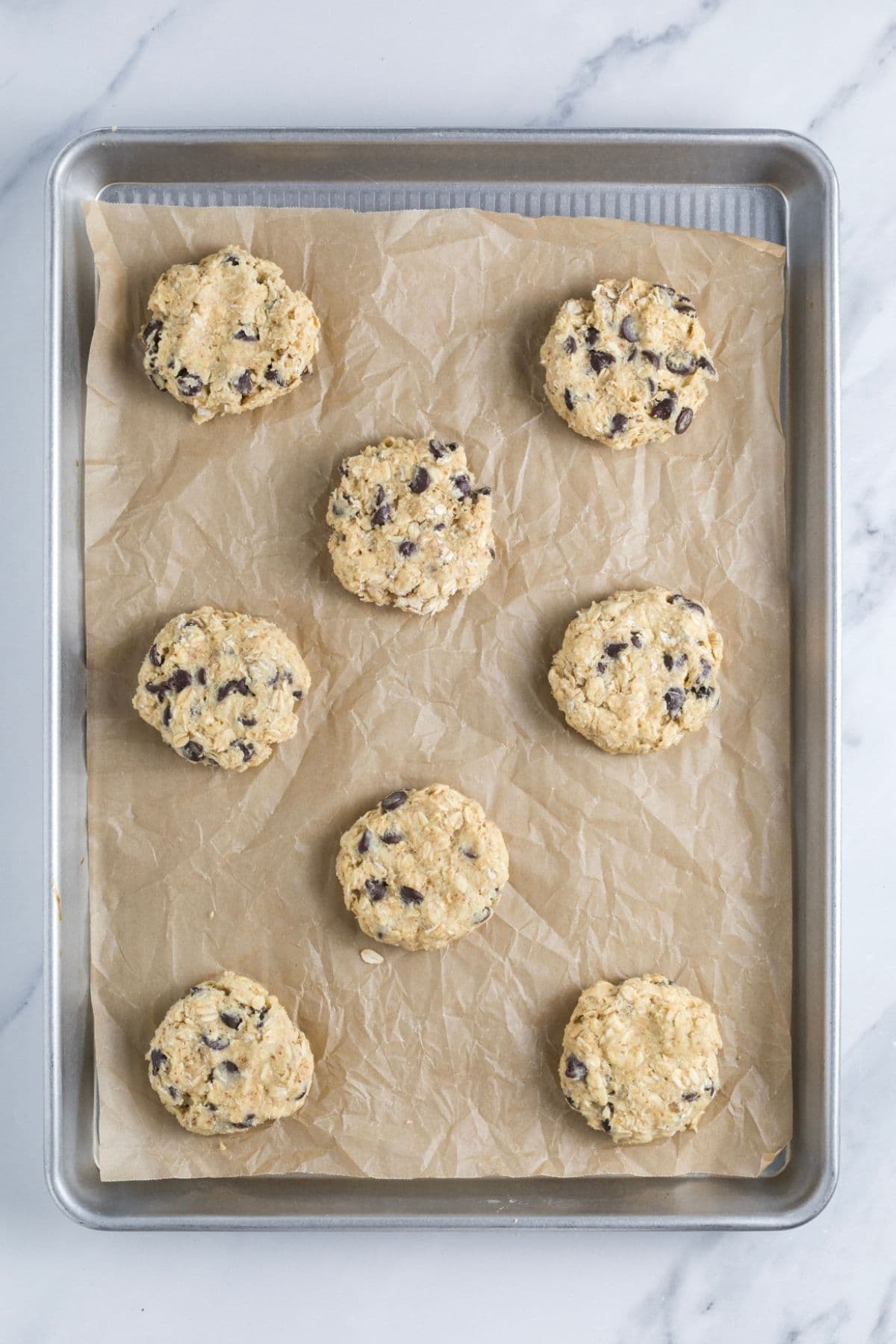 Protein sourdough chocolate chip cookie dough in pieces on a parchment lined baking tray.