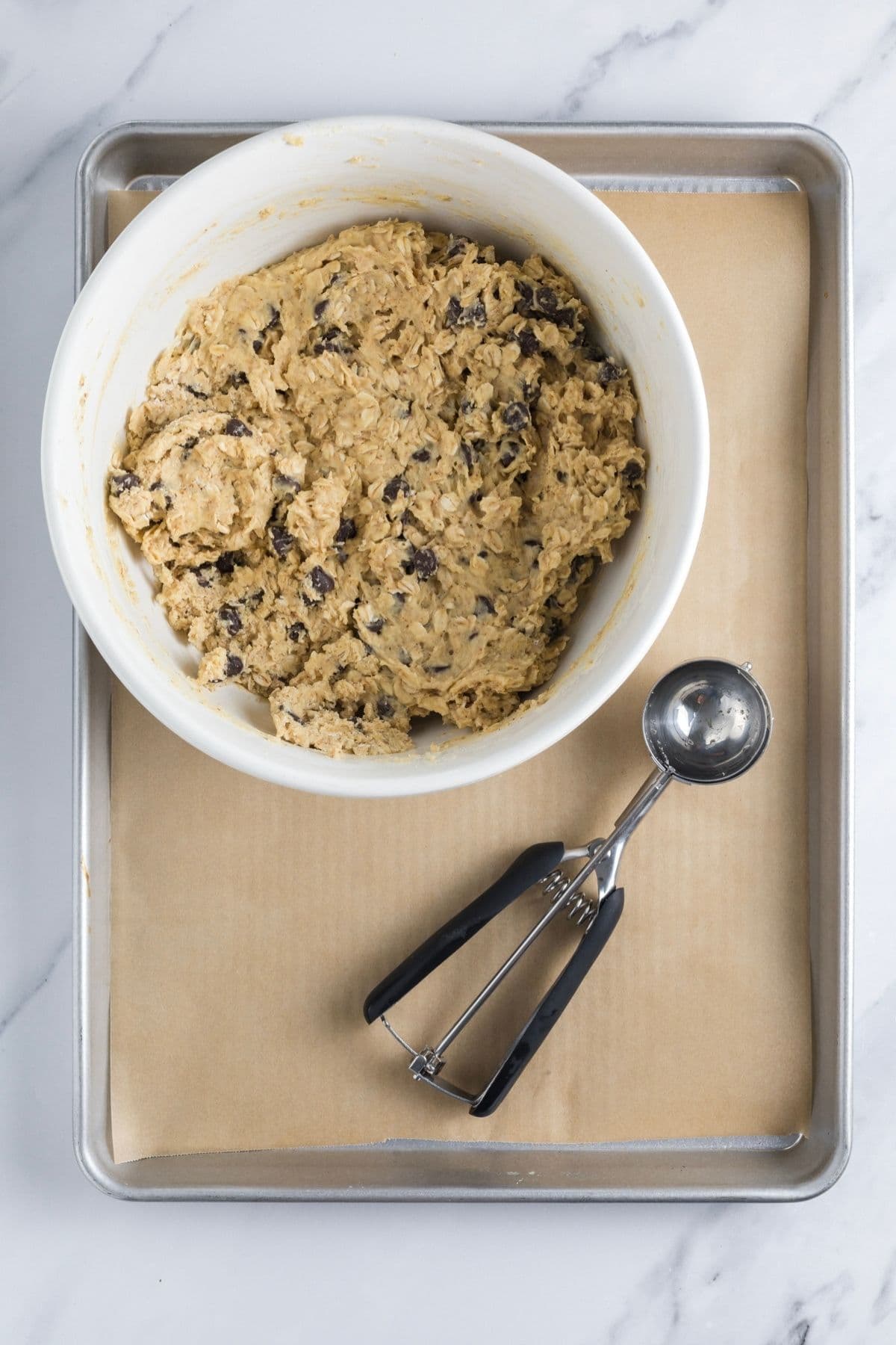 Cookie dough for protein sourdough chocolate chip cookies in a bowl on top of a parchment lined baking tray ready to be added to the tray for baking.