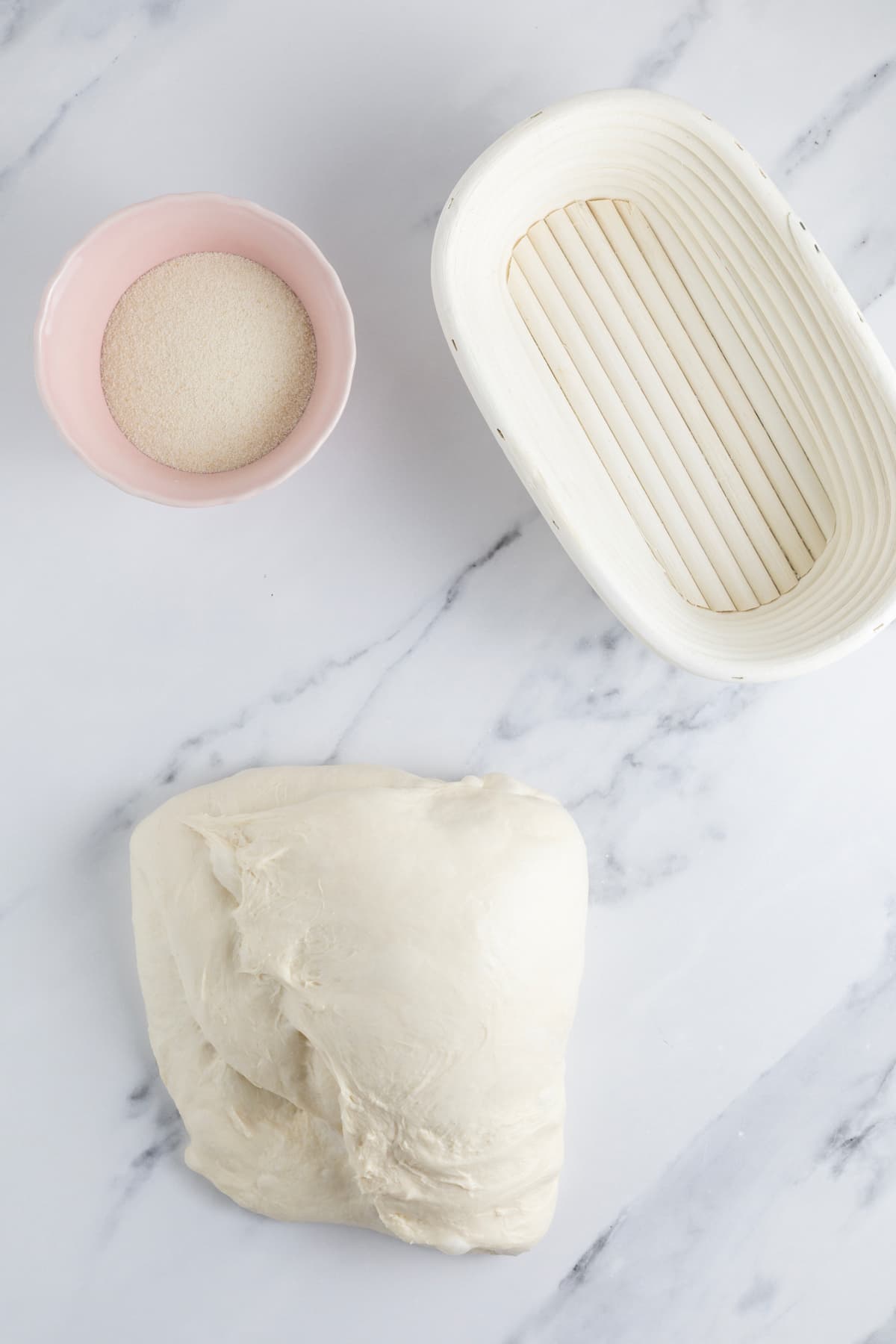 Same day sourdough dough being shaped on a work surface beside a banneton basket and semolina flour before final proofing.