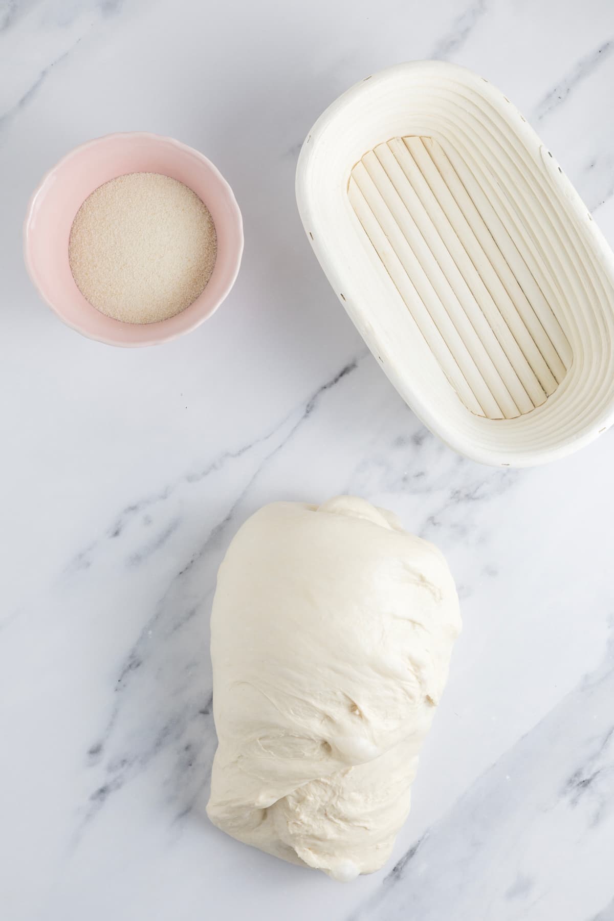 Oval shaped sourdough dough resting beside a proofing basket dusted with semolina flour.