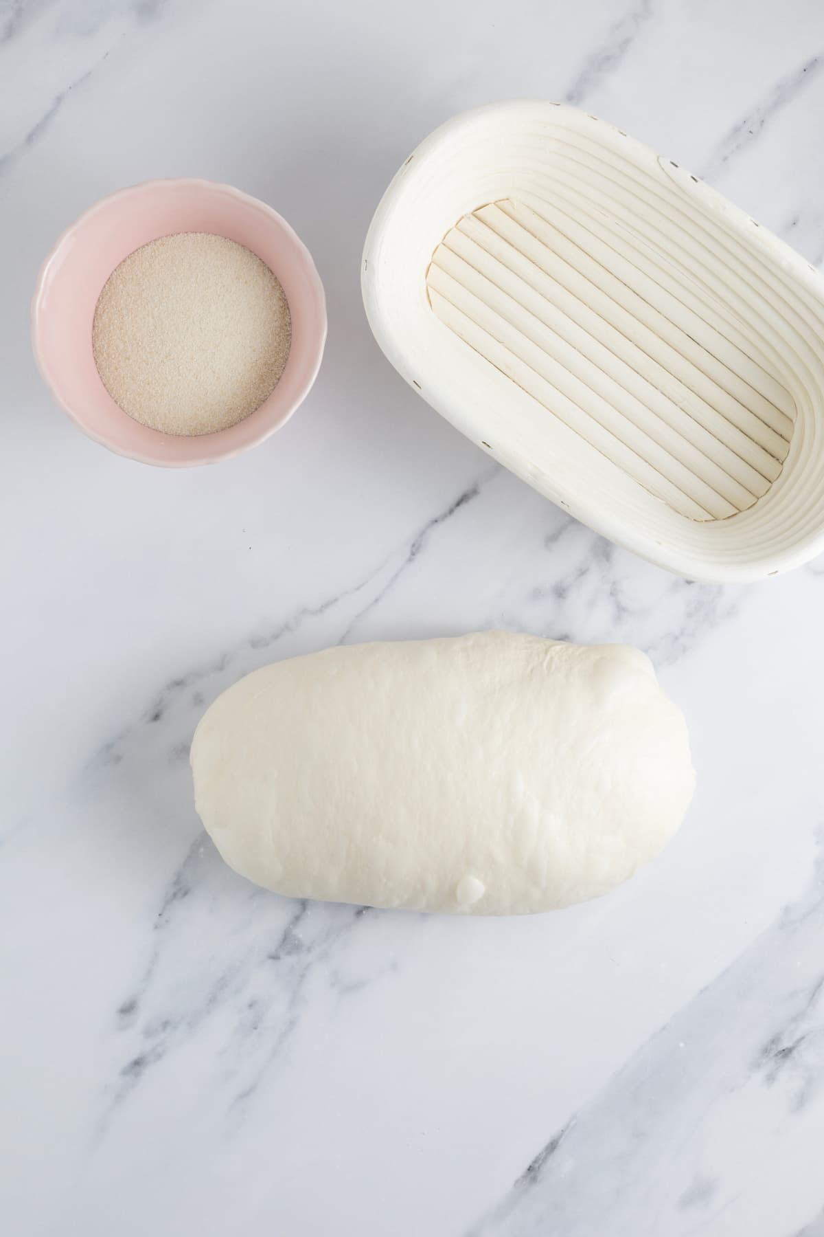 Oval shaped sourdough dough resting beside a proofing basket dusted with semolina flour.