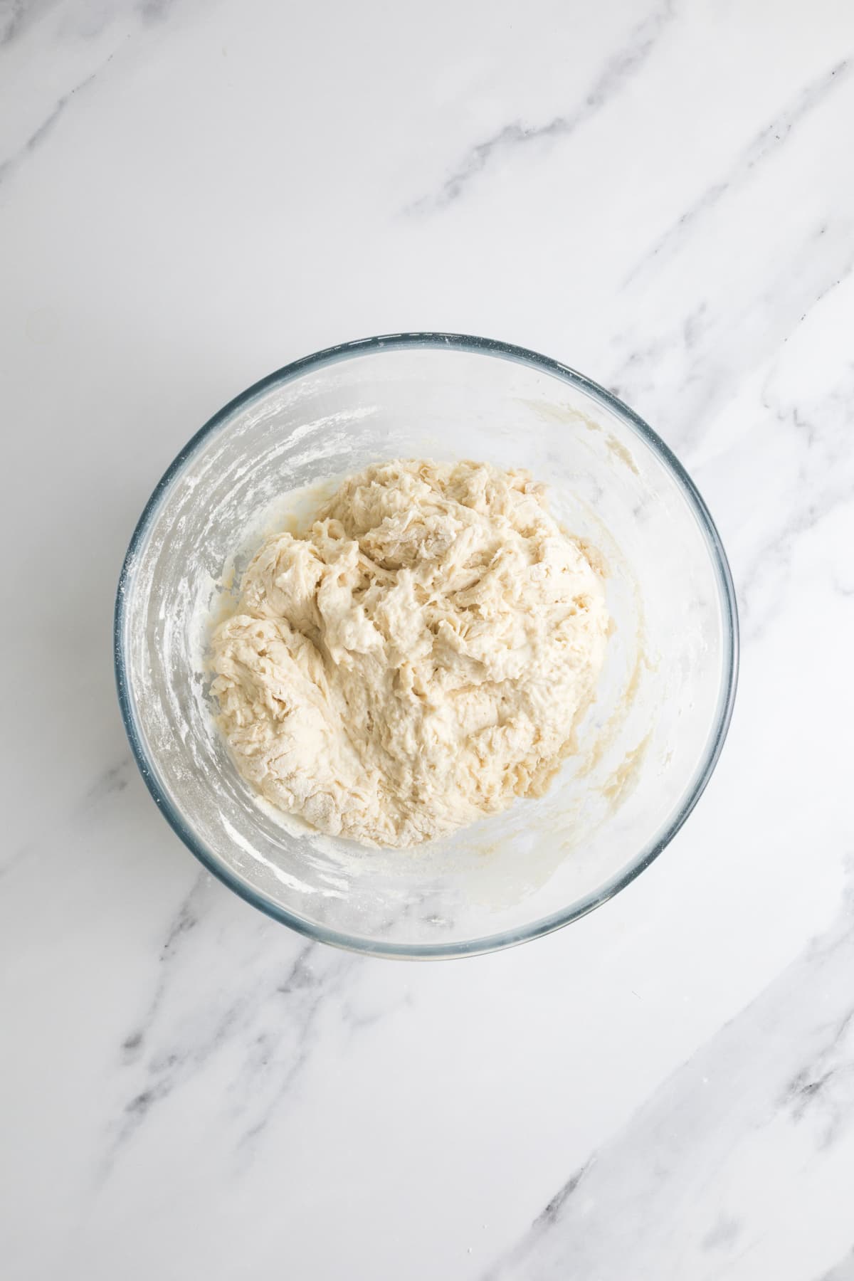 Shaggy sourdough dough in a glass mixing bowl during the early mixing stage.