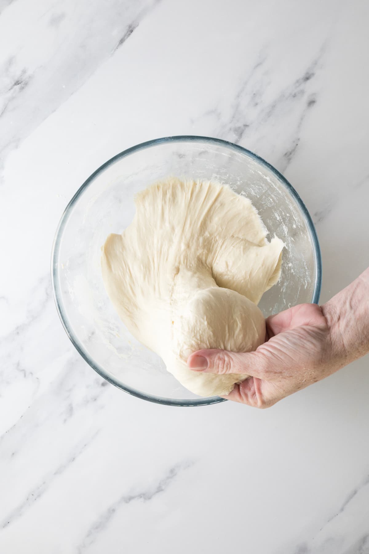 Hand lifting stretchy same day sourdough dough during the strengthening stage before proofing.