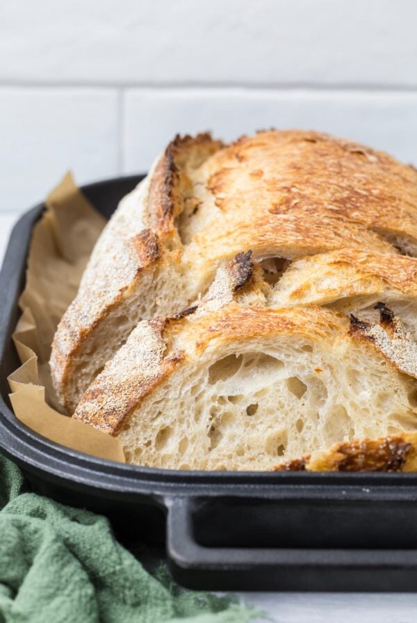 Same day sourdough bread sliced inside a cast iron baker showing an open crumb and crispy crust.