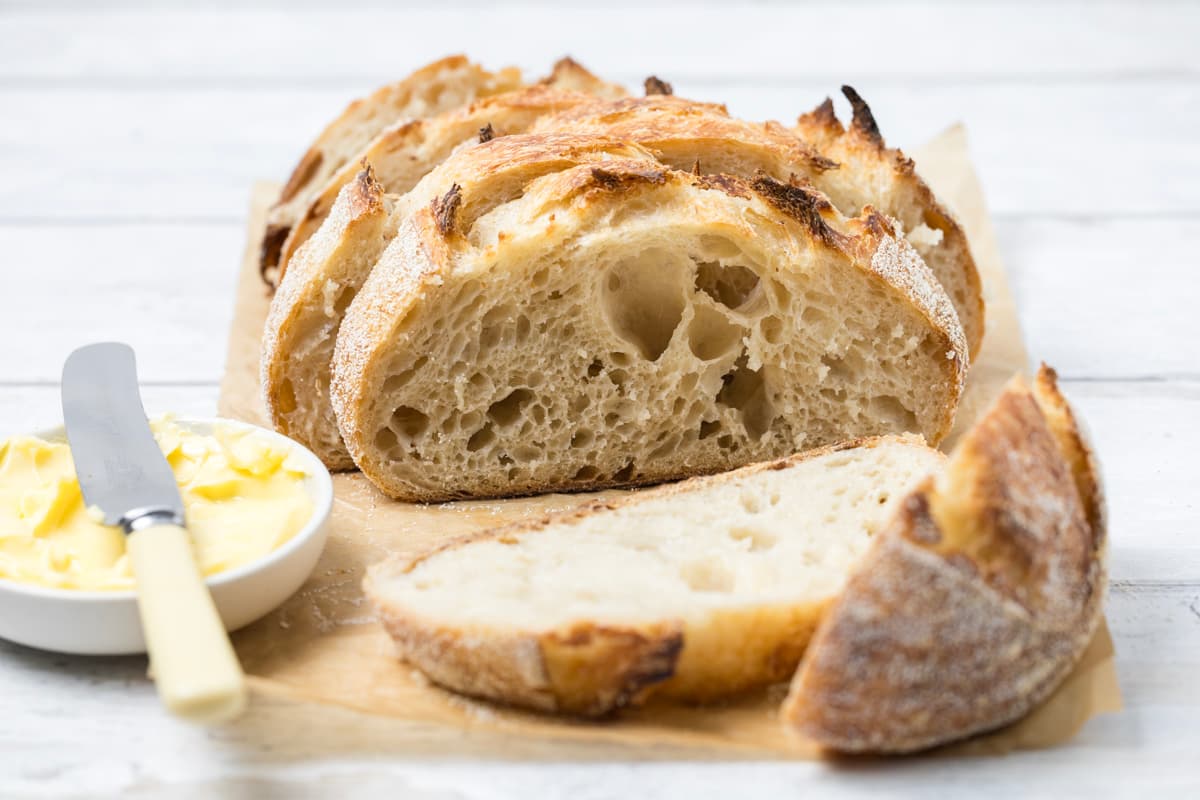 Rustic small batch sourdough bread loaf sliced open on parchment paper with butter and fresh bread slices nearby.