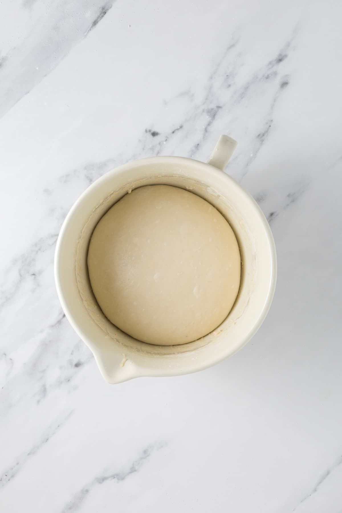Smooth ball of small batch sourdough dough proofing in a ceramic bowl before baking.