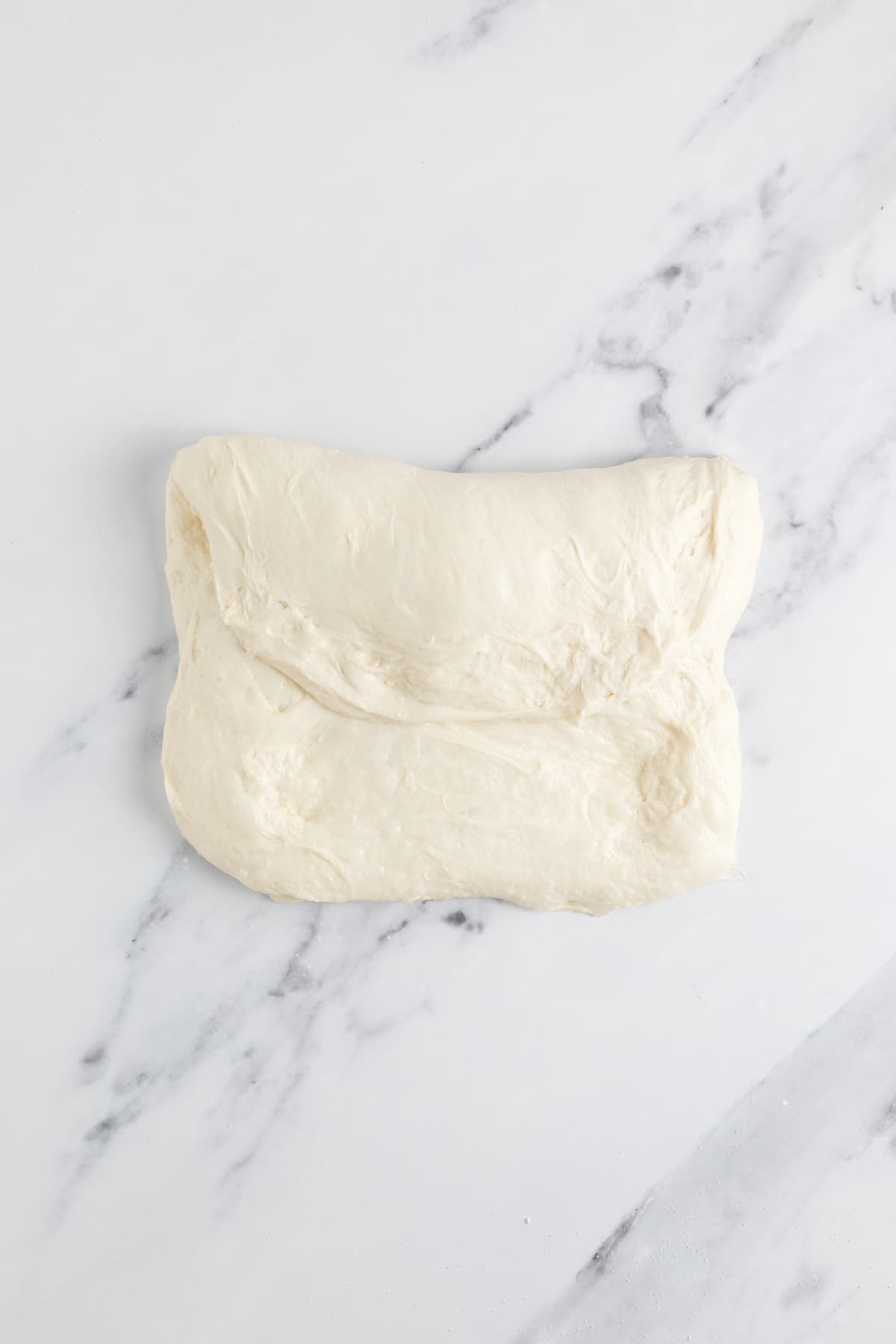 Folded small batch sourdough bread dough during the shaping process on a marble countertop.
