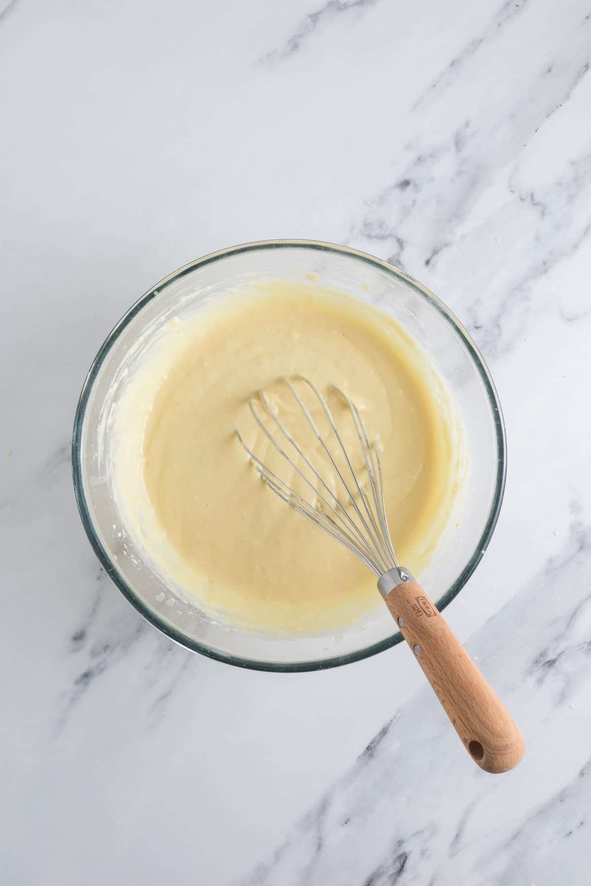Sourdough discard waffle batter in a glass mixing bowl with a whisk.
