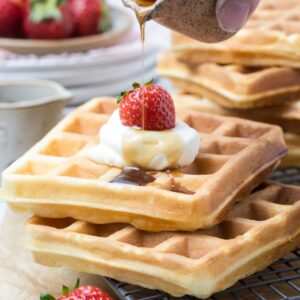Maple syrup drizzled over sourdough discard waffles topped with whipped cream and strawberries.