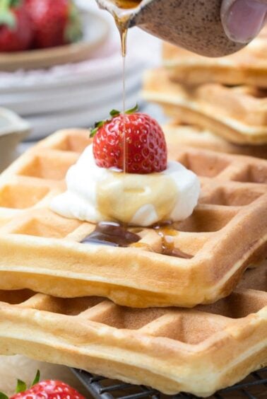 Maple syrup drizzled over sourdough discard waffles topped with whipped cream and strawberries.