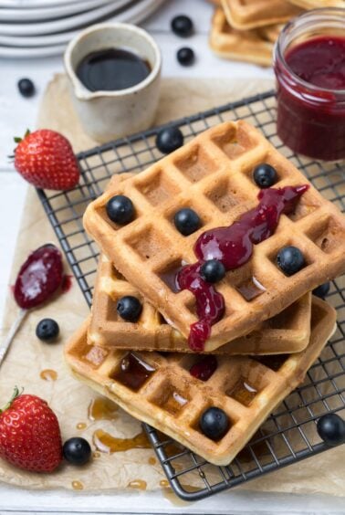 Close up of crispy sourdough discard waffles topped with berry compote, blueberries, and maple syrup.