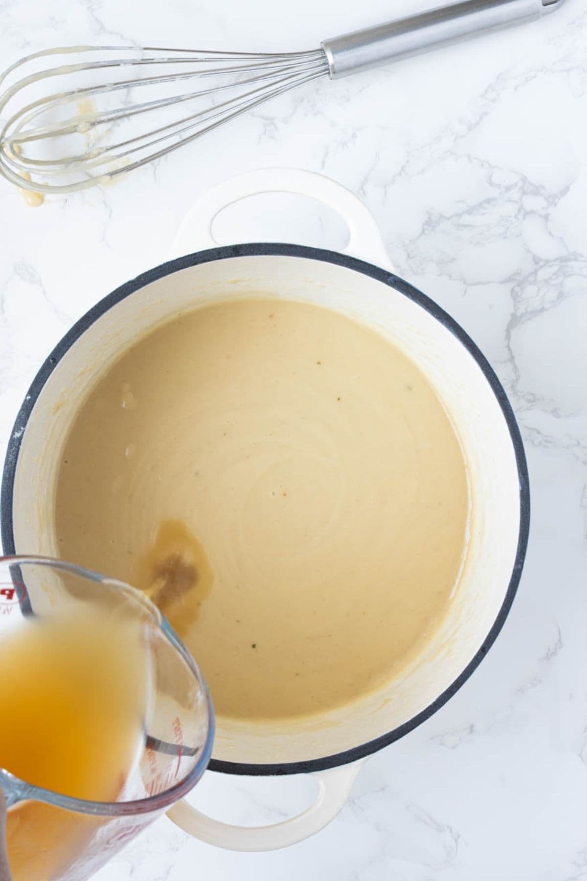 Pouring stock into sourdough gravy mixture while whisking.
