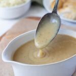 Close up of thick and creamy sourdough gravy dripping from a spoon.