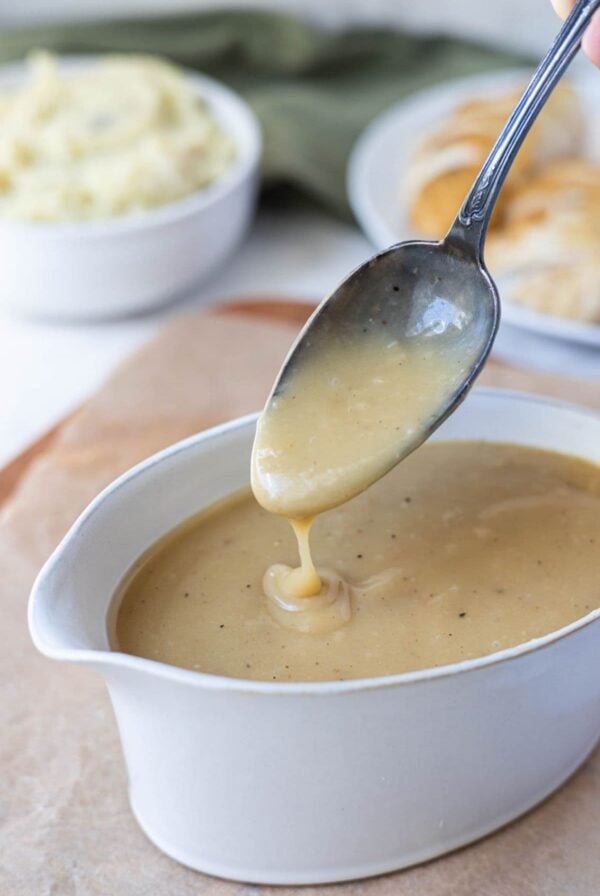 Close up of creamy sourdough gravy dripping from a spoon into a serving dish.