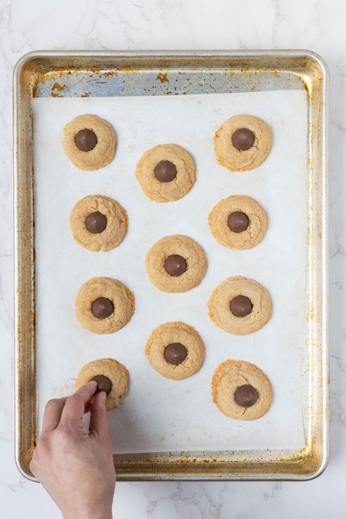 Pressing chocolate kisses into warm sourdough peanut butter blossom cookies on a baking sheet.