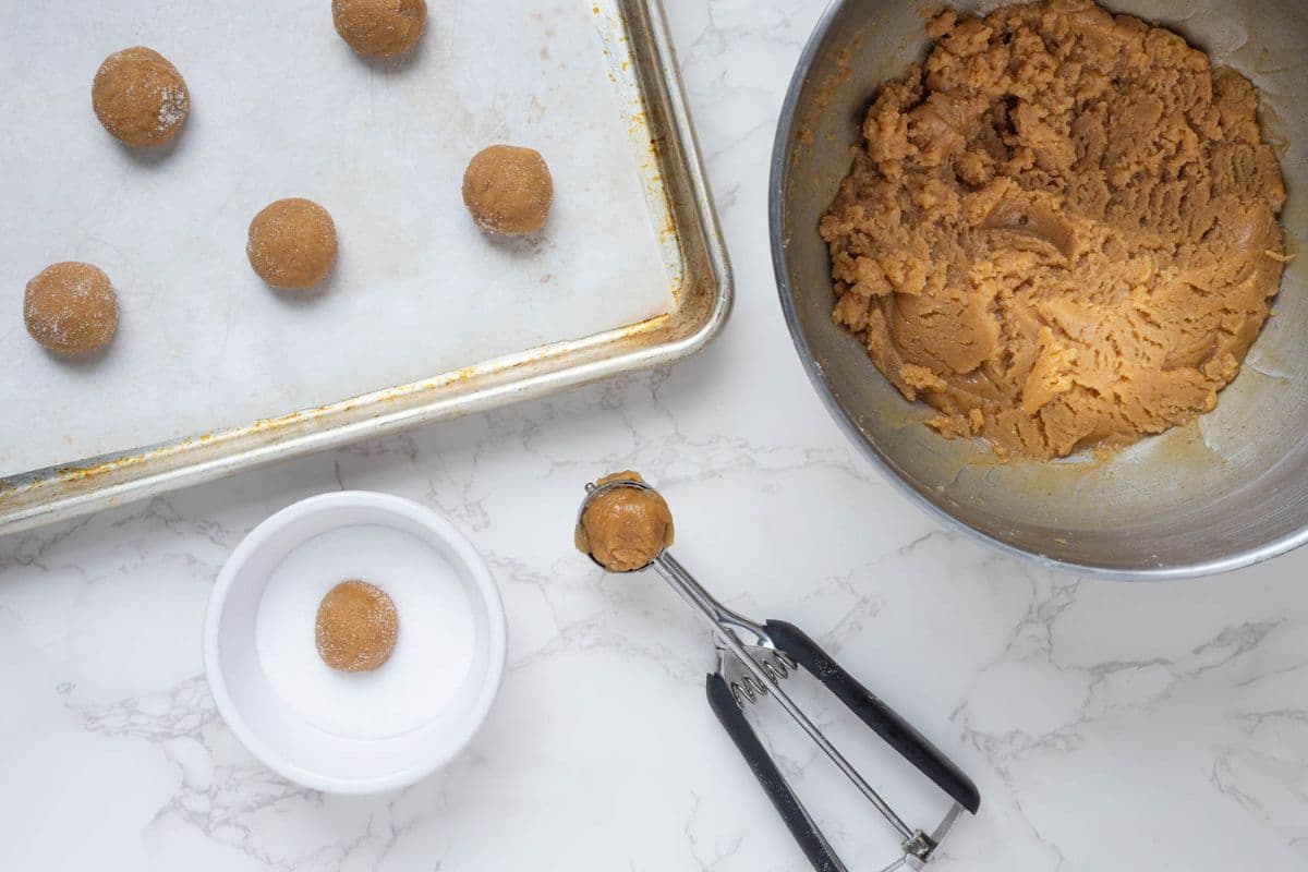 Rolling sourdough peanut butter cookie dough balls in sugar before baking.