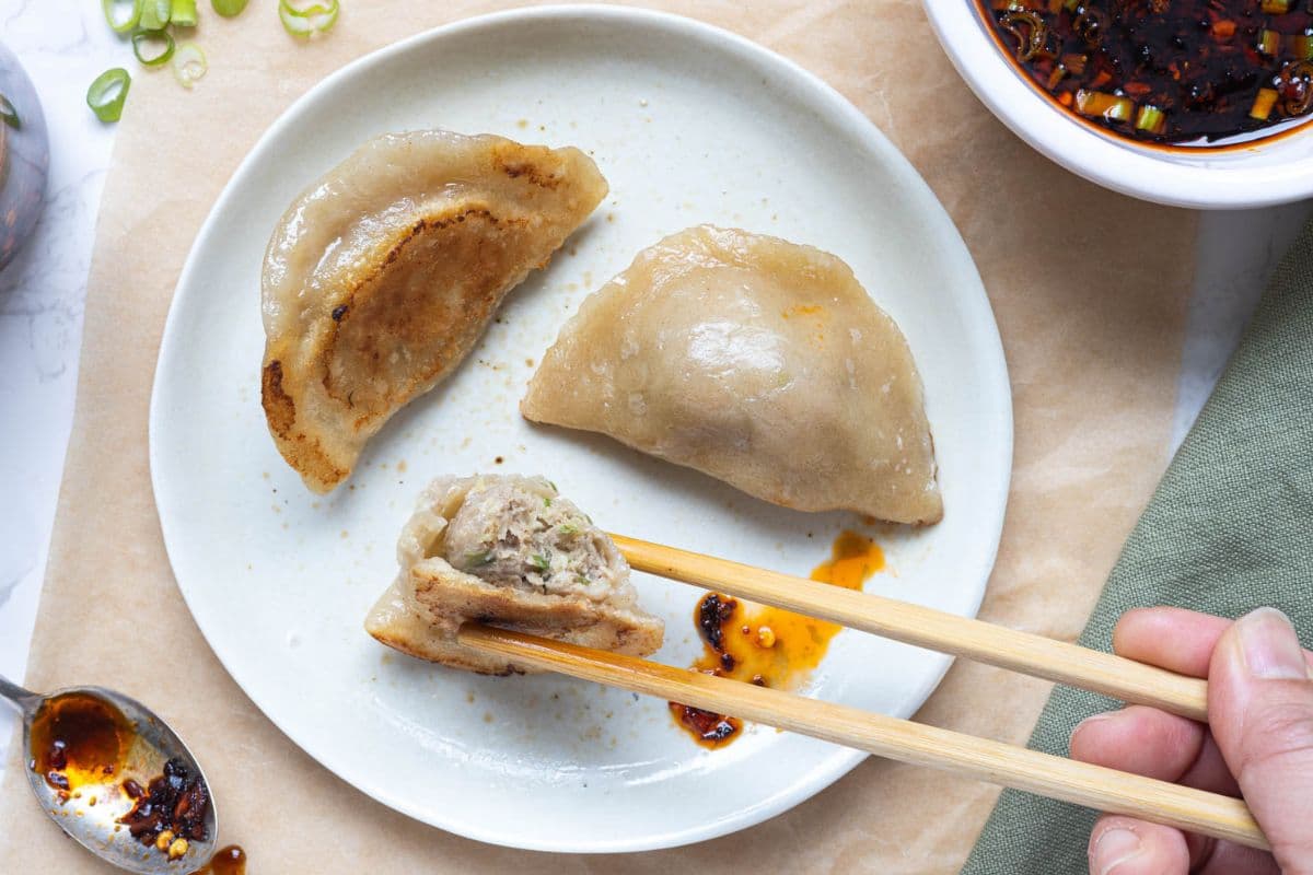 A plate of sourdough potstickers with a bite taken out of one while eating with chopsticks.