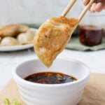 Crispy homemade sourdough potsticker held with chopsticks above spicy dipping sauce.