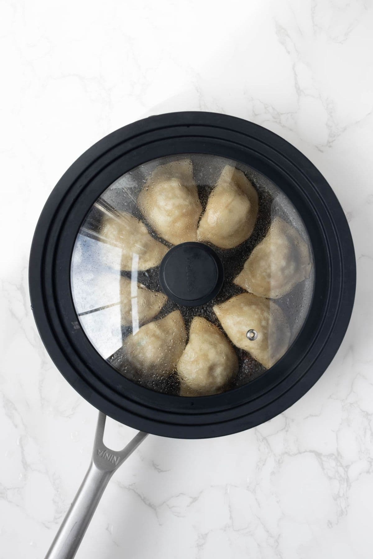 Sourdough potstickers steaming in a covered skillet.