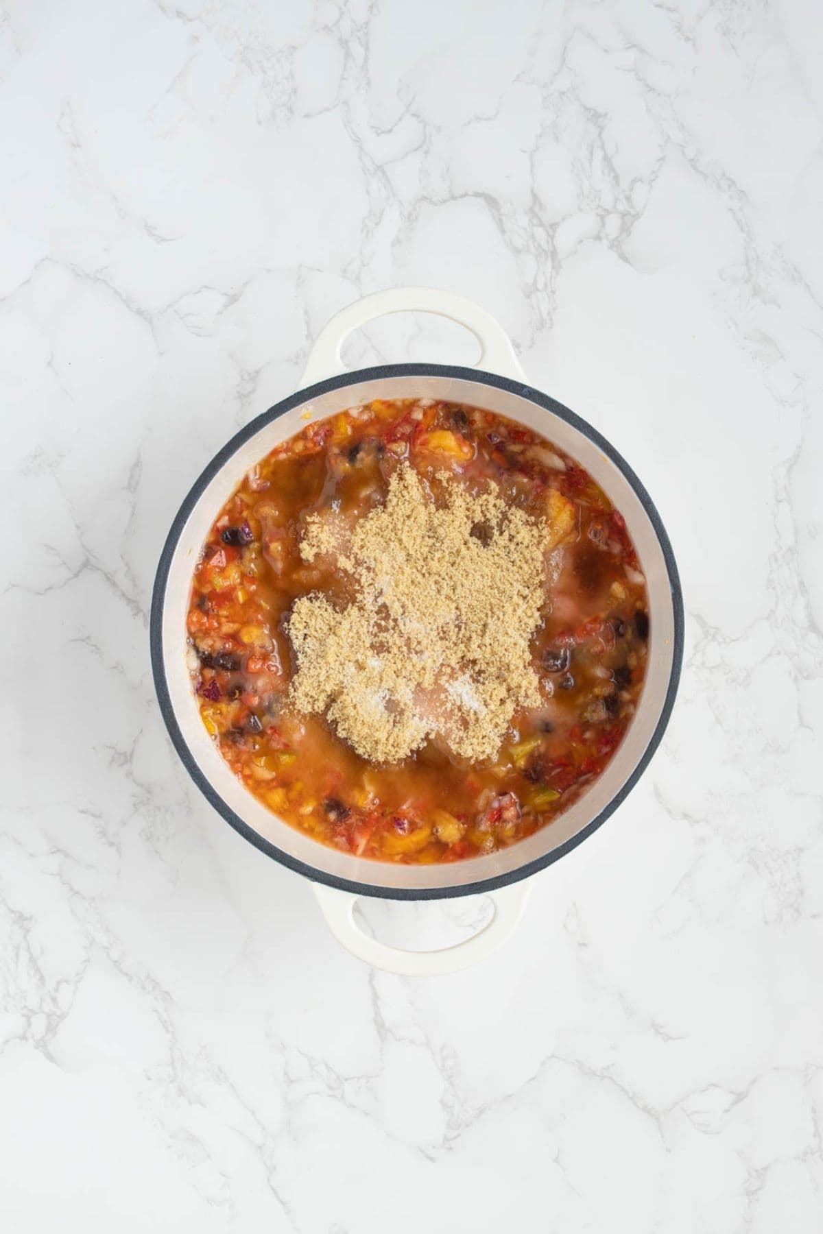 Seasonings being added to summer fruits relish in a pot before cooking.