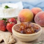 Bowl of summer fruits relish served with with sourdough crackers and fruit on a wooden board.