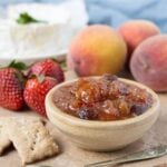 Summer fruits relish in a small bowl served with strawberries, peaches, sourdough crackers, and soft cheese.
