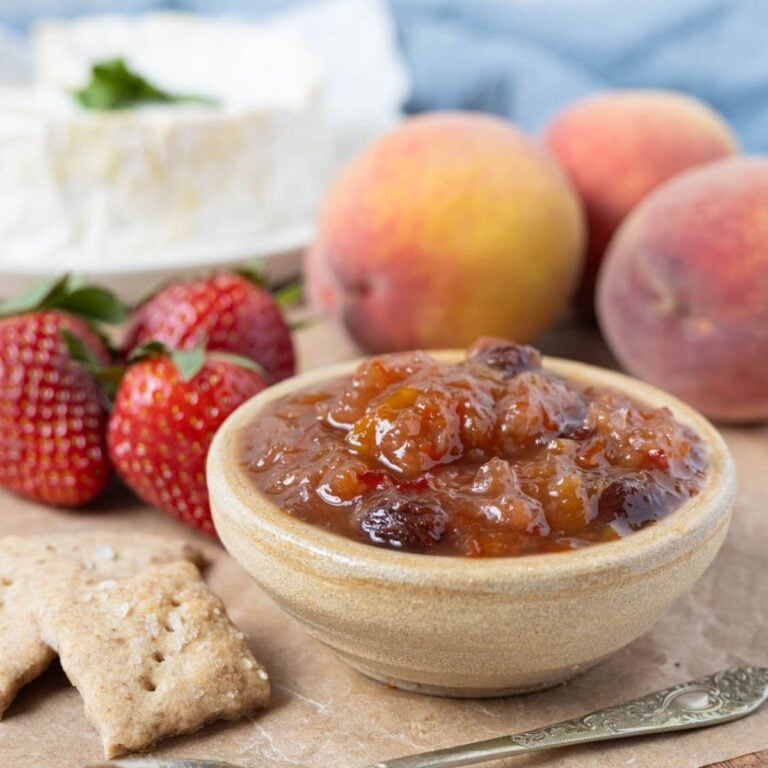 Summer fruits relish in a small bowl served with strawberries, peaches, sourdough crackers, and soft cheese.