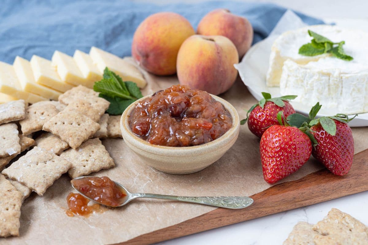 Bowl of summer fruits relish served with sourdough crackers, strawberries, peaches, and brie cheese.