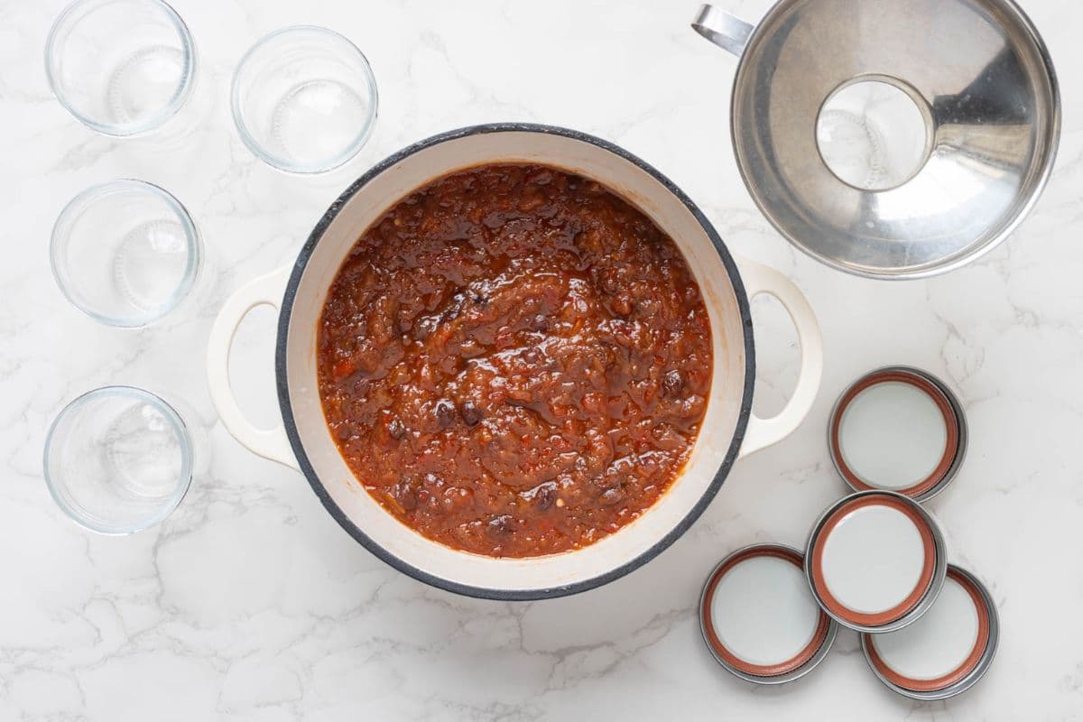 Cooked summer fruits relish in a pot beside clean jars and lids ready for storing.