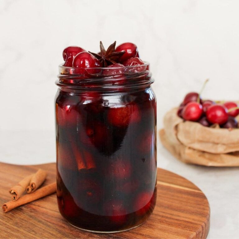 Sweet pickled cherries in a glass jar with cinnamon sticks and star anise in a spiced vinegar brine.