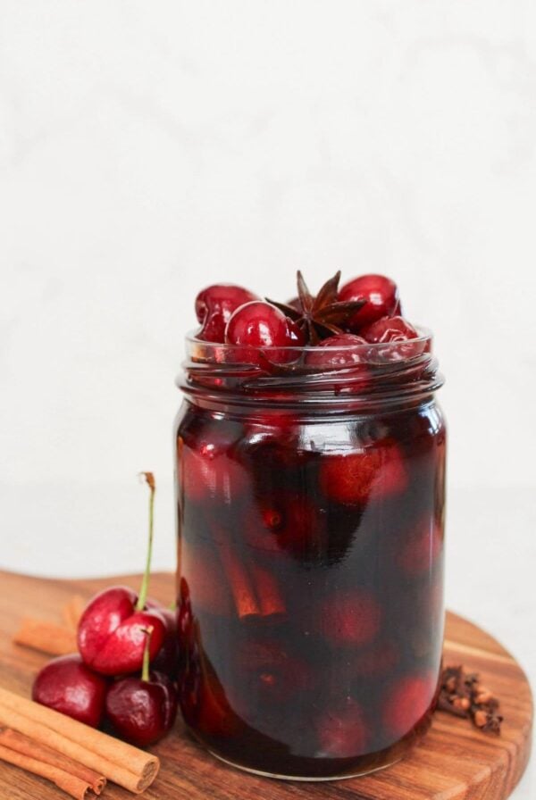 Homemade sweet pickled cherries preserved in a glass jar with warm spices and vinegar brine.