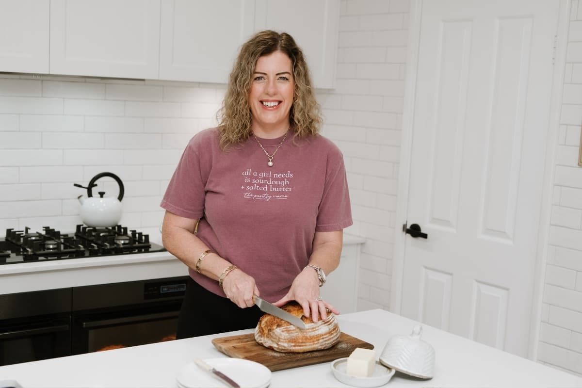 Kate Freebairn, founder of The Pantry Mama standing in her kitchen and slicing a loaf of sourdough bread.