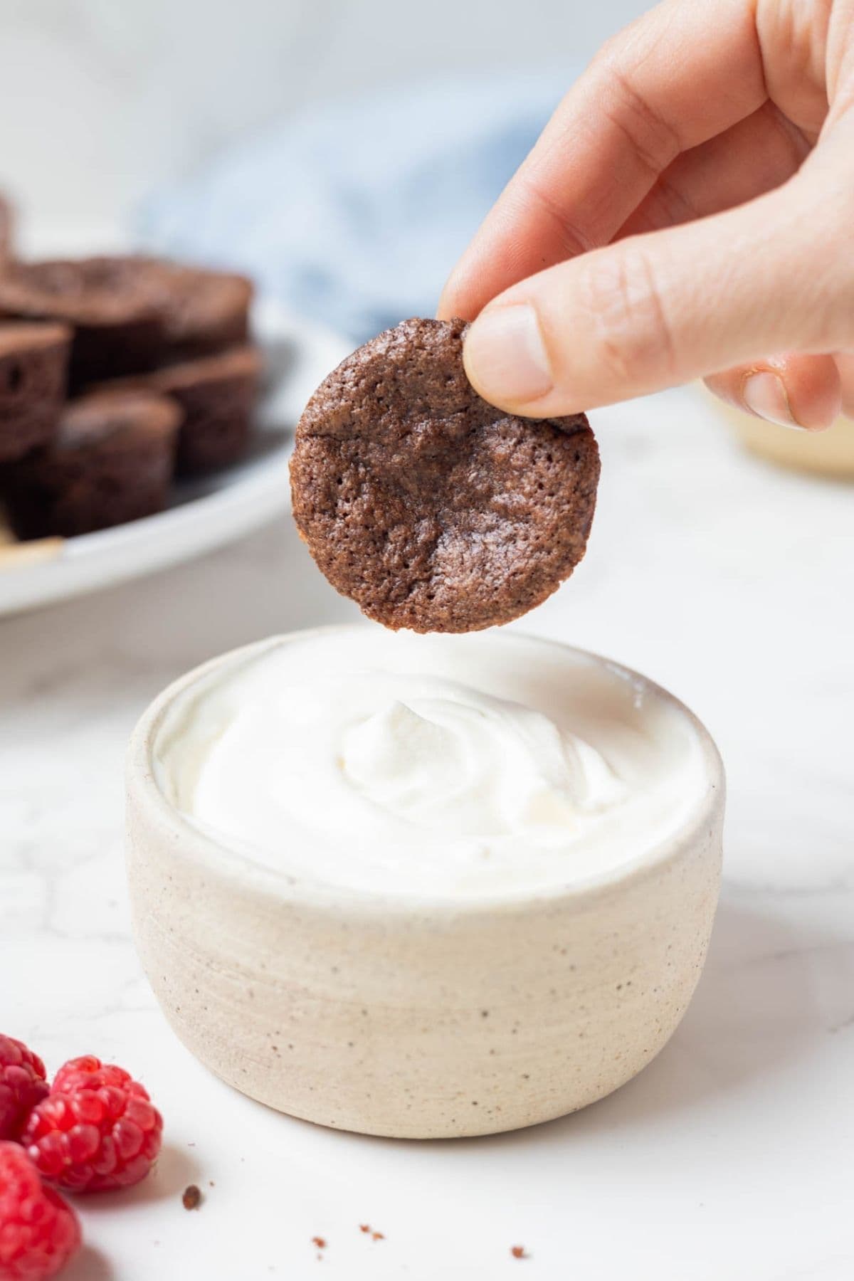 Sourdough chocolate brownie bite being dipped into whipped cream before serving.