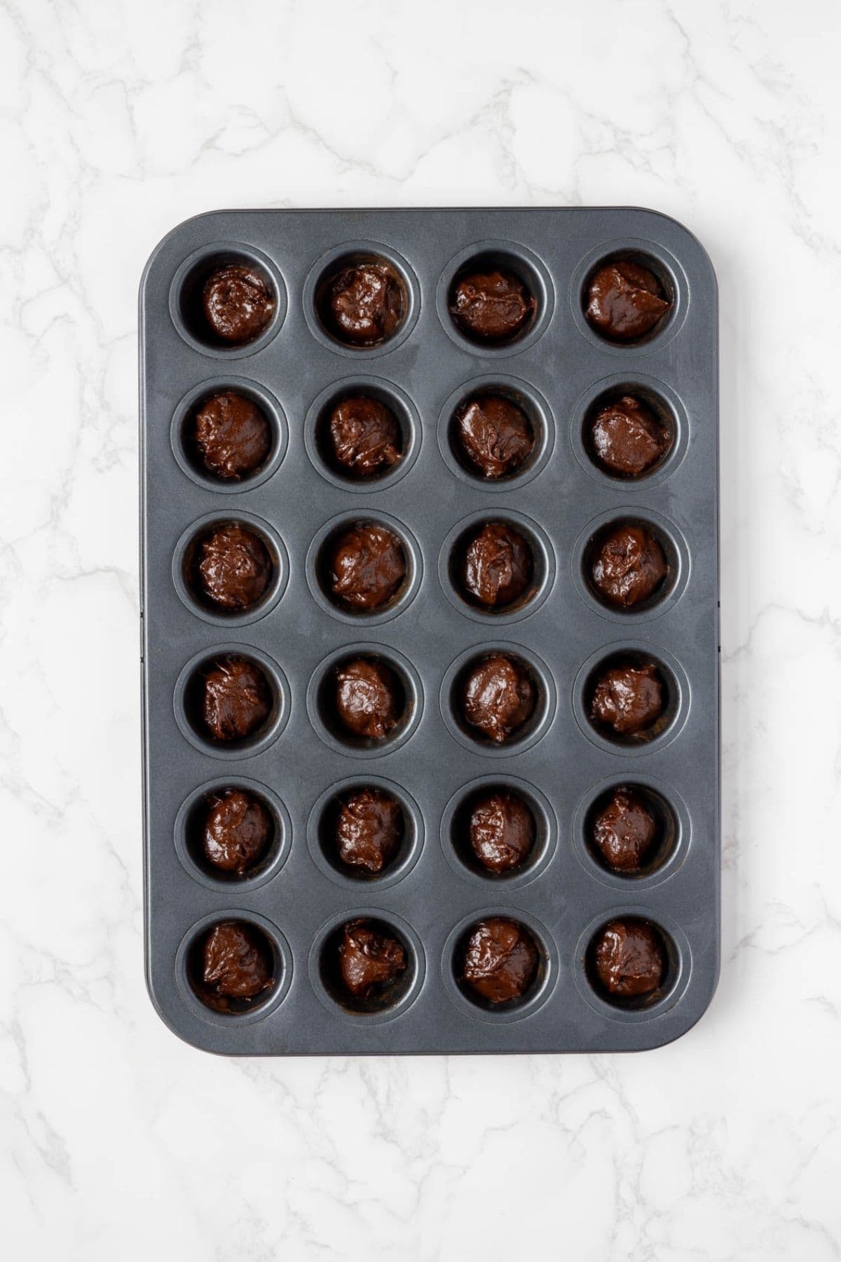 Sourdough chocolate brownie batter portioned into a mini muffin pan before baking.