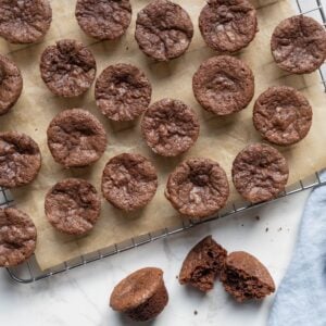 Sourdough chocolate brownie bites cooling on a wire rack with one brownie bite broken open to show the inside texture.