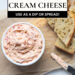 Creamy roasted red pepper cream cheese served with sliced sourdough bread on a wooden board.
