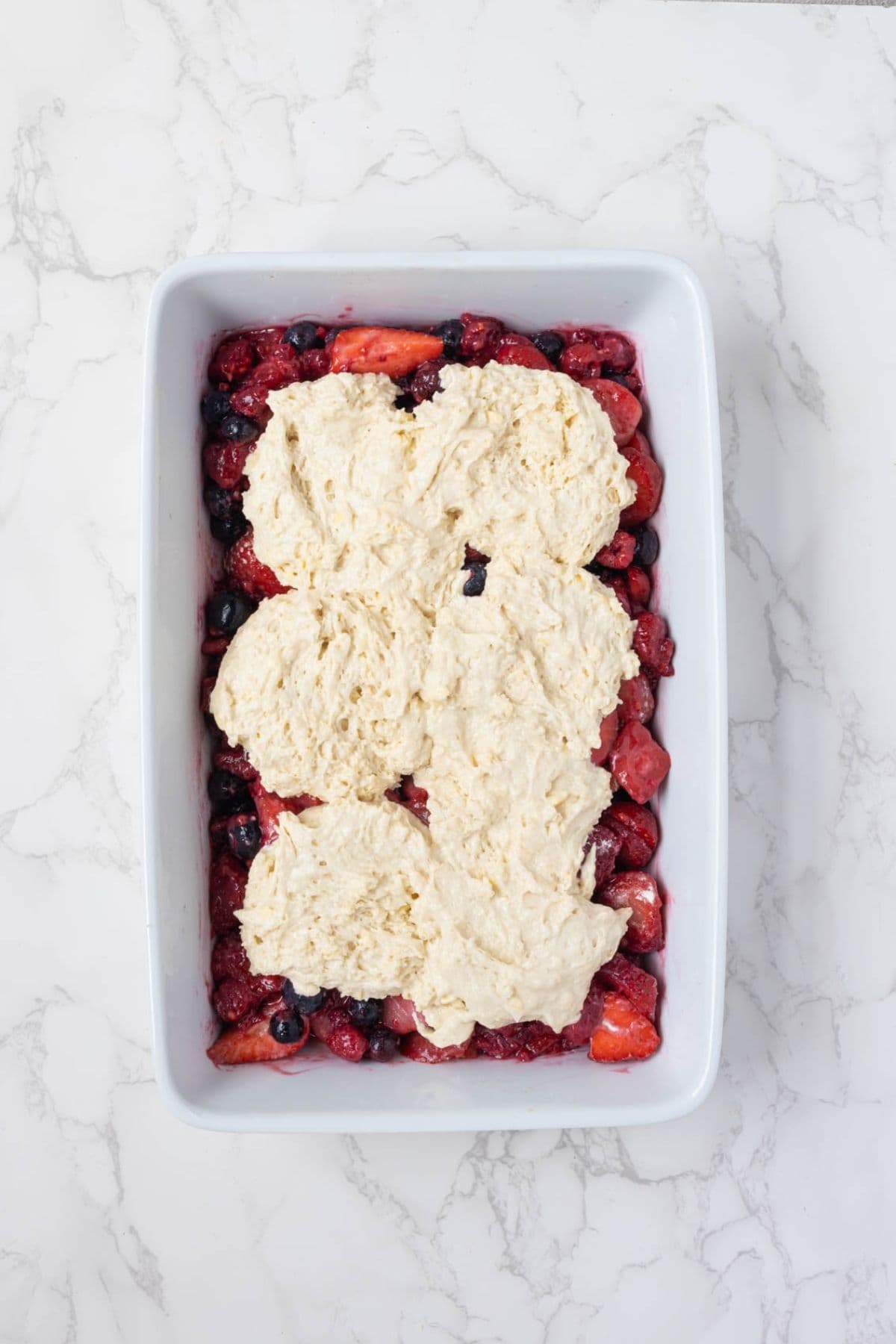 Sourdough cobbler topping spread over mixed berry filling before baking.