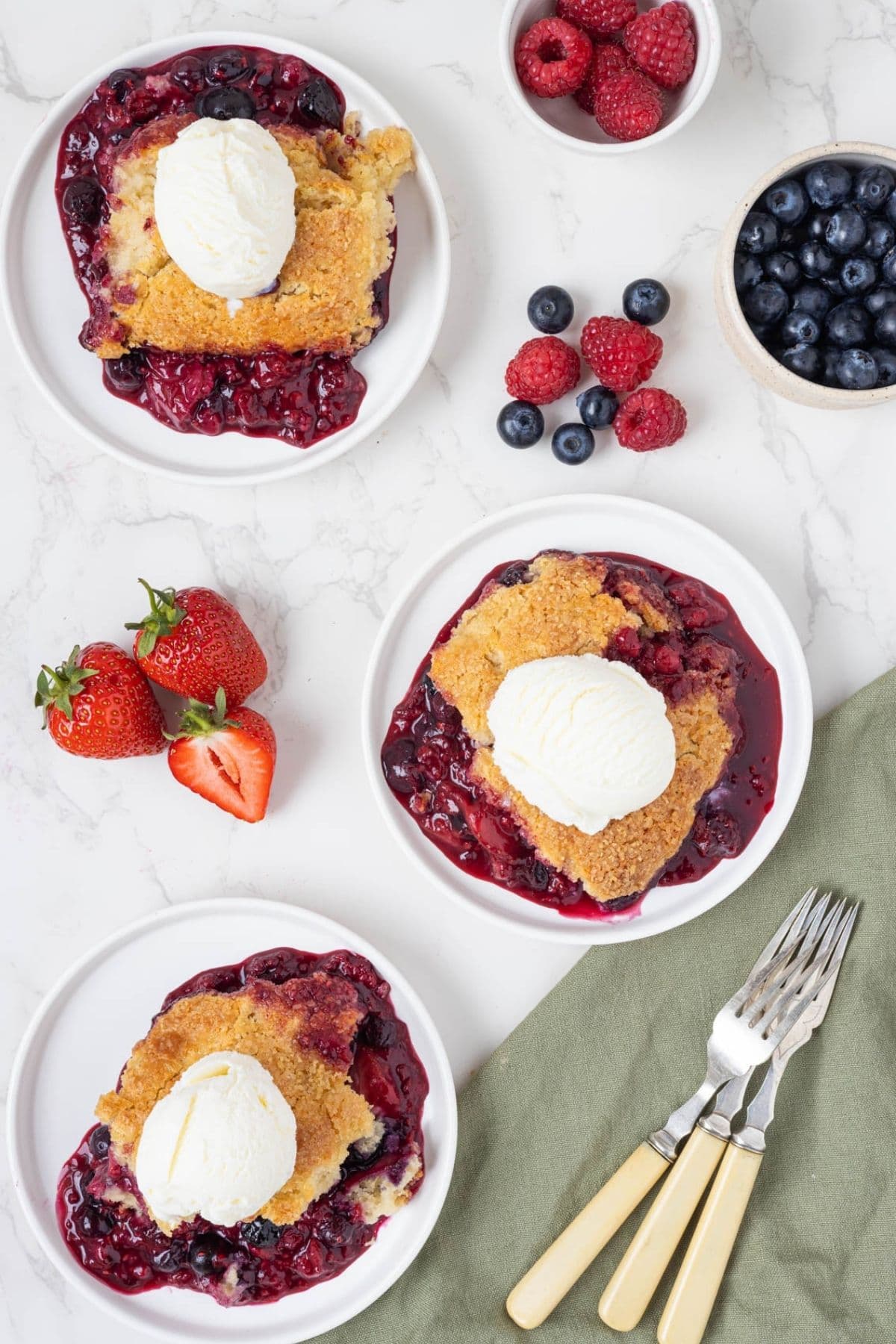 Three servings of sourdough berry cobbler topped with vanilla ice cream and arranged for serving.