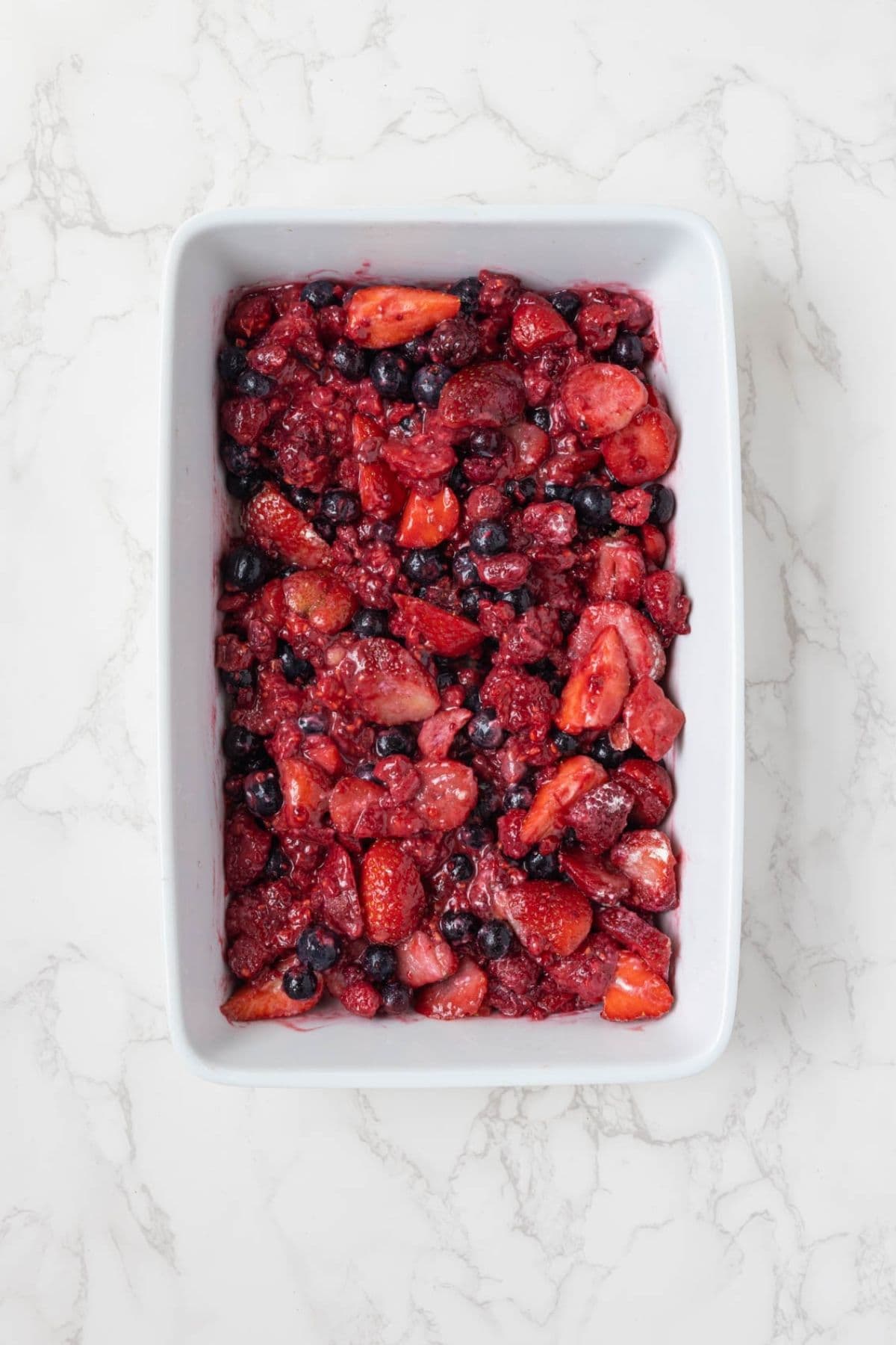 Mixed berry cobbler filling made with strawberries, raspberries, and blueberries in a baking dish.