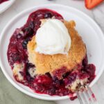 Single serving of sourdough berry cobbler topped with vanilla ice cream and surrounded by mixed berry filling.