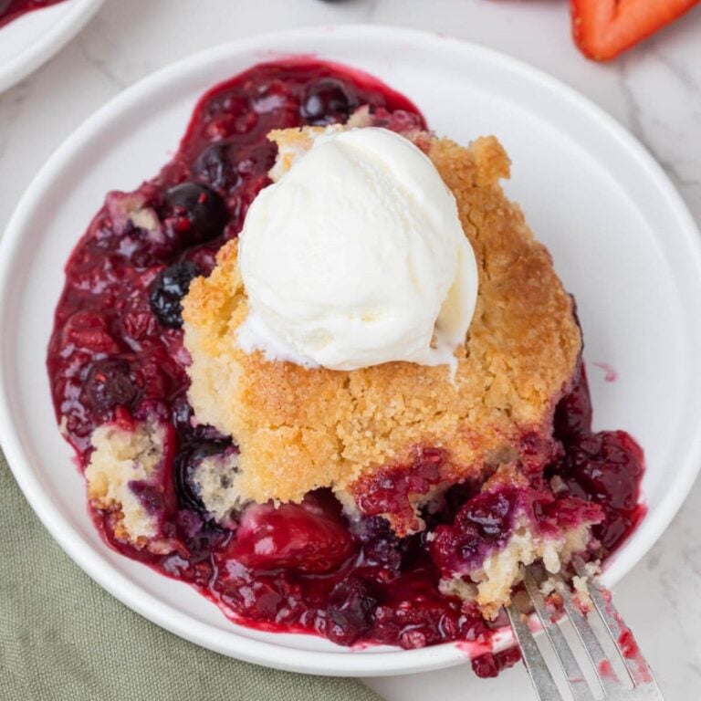 Single serving of sourdough berry cobbler topped with vanilla ice cream and surrounded by mixed berry filling.