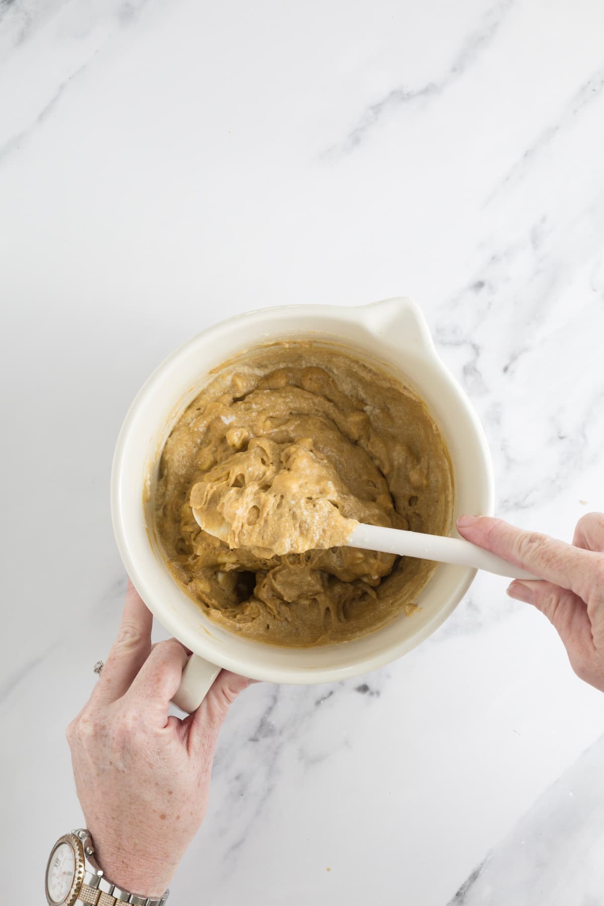 Overhead view of hands folding whipped egg whites into sourdough blondie batter.