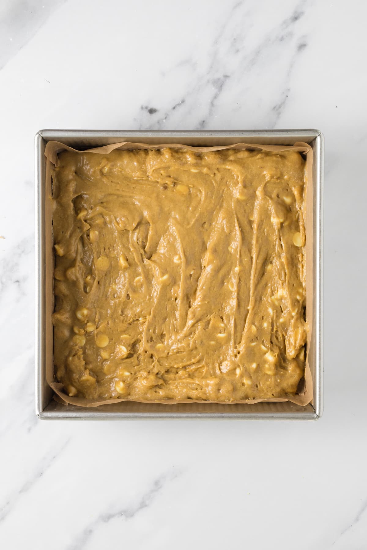 Sourdough blondie batter spread into a parchment lined baking pan before baking.