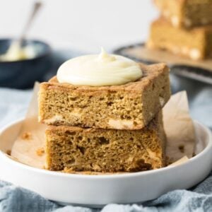 Sourdough blondies stacked on a plate and topped with frosting.