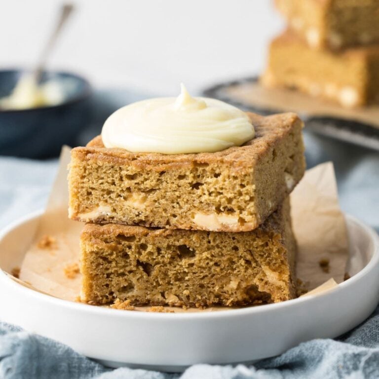 Sourdough blondies stacked on a plate and topped with frosting.