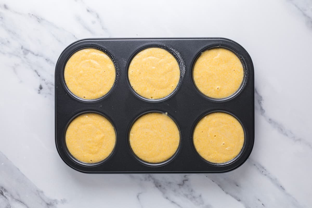 Sourdough cornbread muffin batter portioned evenly into six muffin cups before baking.