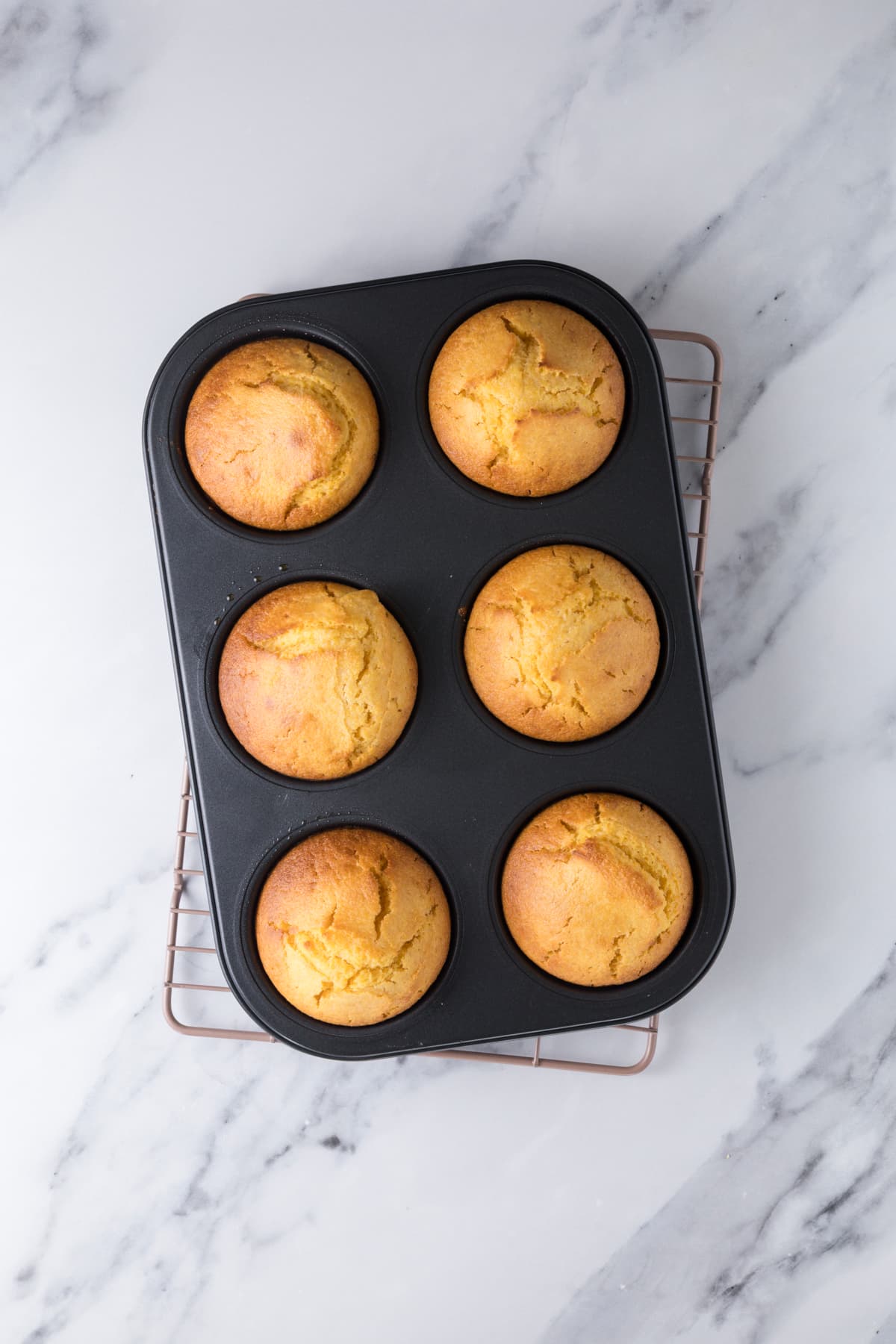 Freshly baked sourdough cornbread muffins cooling in a muffin tin after being removed from the oven.
