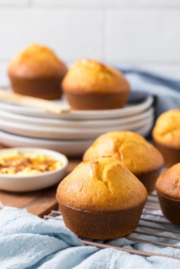 Several sourdough cornbread muffins on a cooling rack with one muffin positioned in the foreground.